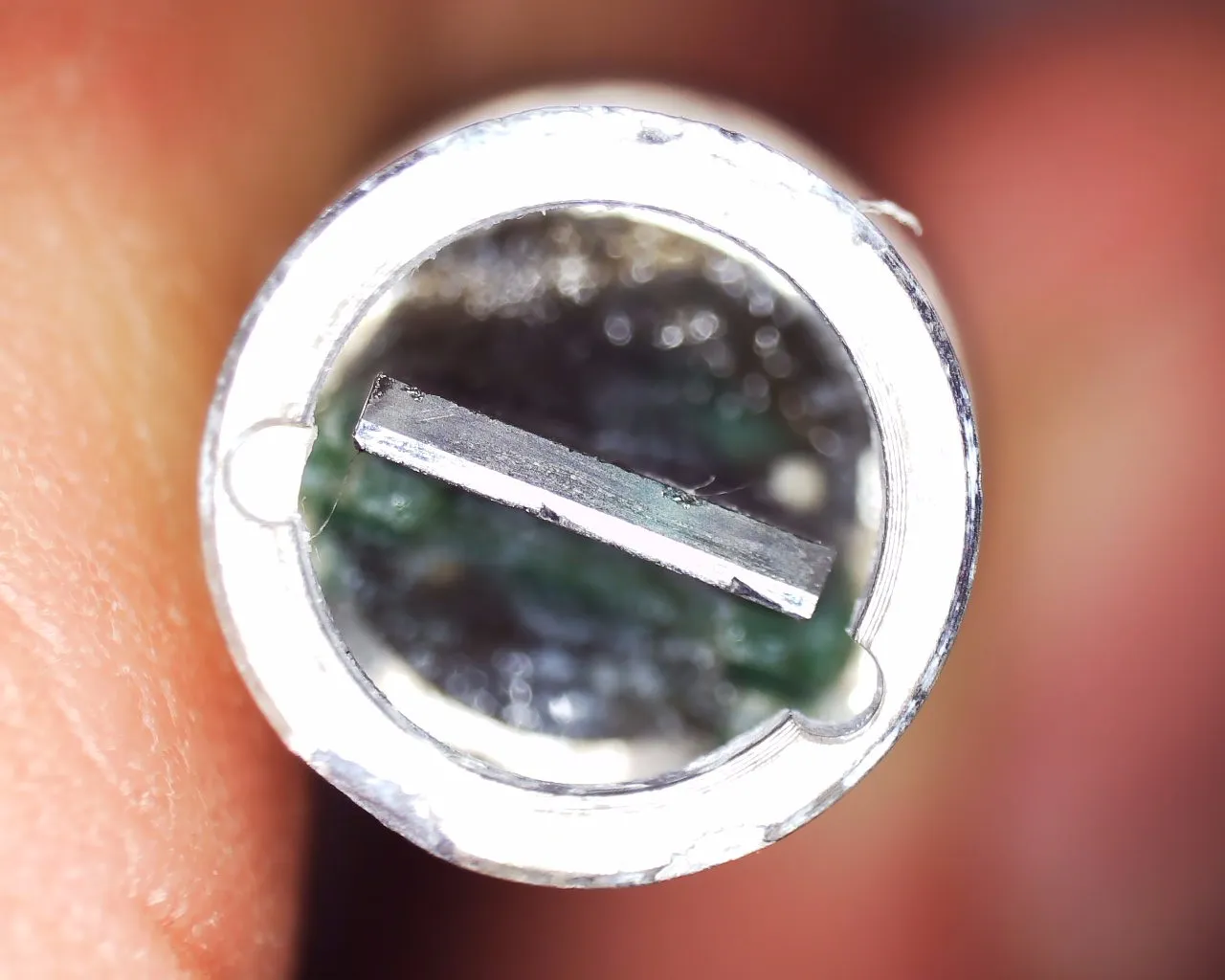 A microscopic image of a round and hollow metal instrument. In the middle is a horizontal bar